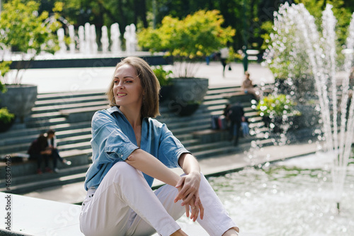 Urban portrait of young attractive business woman in eye glasses and casual clothes. Woman walking in the city street, green park, reading a book, relax, works in sunny day.