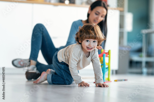 Young beautiful mother playing on the floor with her son in living room at home.