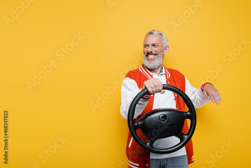 Canvas Print happy middle aged man in bomber jacket holding steering wheel while gesturing is