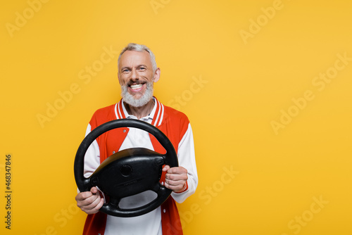 Tableau sur toile joyful middle aged man in bomber jacket holding steering wheel while imitating d