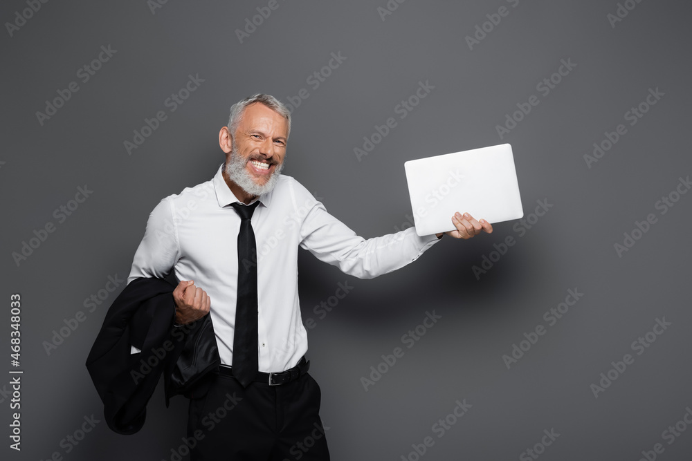 happy middle aged businessman holding laptop and blazer on grey happy middle aged businessman holding laptop and blazer on grey
