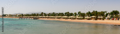 Hurghada, Egypt - September 22, 2021: Panoramic view of the Red Sea coast. People are relaxing and swimming on a sandy beach with green palm trees.