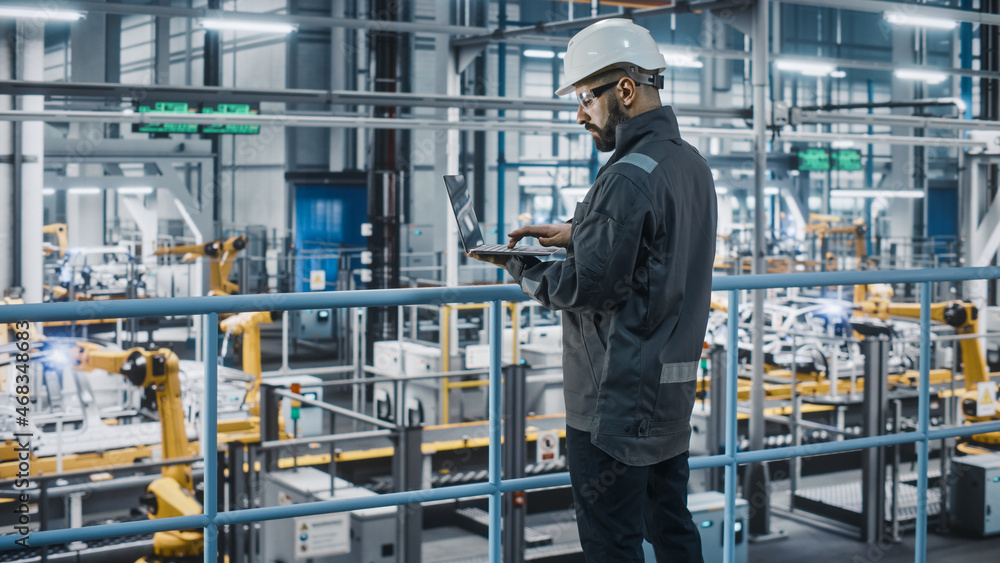 Car Factory Engineer in Work Uniform Using Laptop Computer. Automotive Industrial Manufacturing Facility Working on Vehicle Production with Robotic Arms Technology. Automated Assembly Plant. Car Factory Engineer in Work Uniform Using Laptop Computer. Automotive Industrial Manufacturing Facility Working on Vehicle Production with Robotic Arms Technology. Automated Assembly Plant.