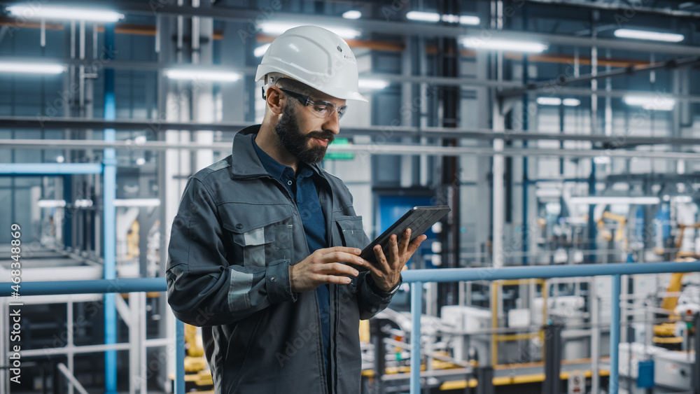 Car Factory Engineer in Work Uniform Using Tablet Computer. Automotive Industry 4.0 Manufacturing Facility Working on Vehicle Production with Robotic Arms Technology. Automated Assembly Plant. Car Factory Engineer in Work Uniform Using Tablet Computer. Automotive Industry 4.0 Manufacturing Facility Working on Vehicle Production with Robotic Arms Technology. Automated Assembly Plant.