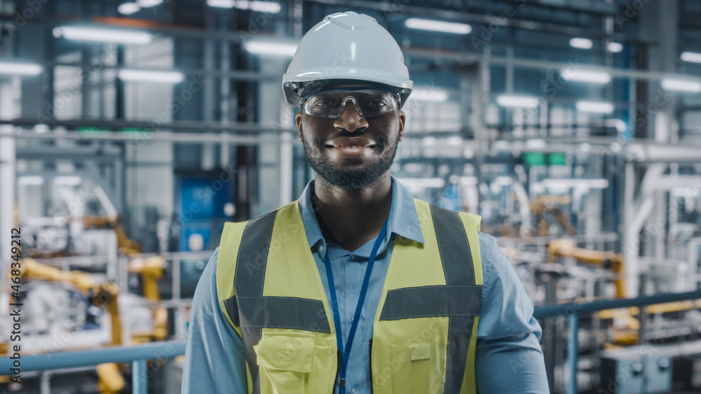 Portrait of an Automotive Industry Engineer in Safety Uniform Smiling at Car Factory Facility. Happy Assembly Plant African American Male Specialist Working on Manufacturing Modern Electric Vehicles. Portrait of an Automotive Industry Engineer in Safety Uniform Smiling at Car Factory Facility. Happy Assembly Plant African American Male Specialist Working on Manufacturing Modern Electric Vehicles.