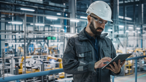 Car Factory Engineer in Work Uniform Using Tablet Computer. Automotive Industrial Manufacturing Facility Working on Vehicle Production with Robotic Arms Technology. Automated Assembly Plant.