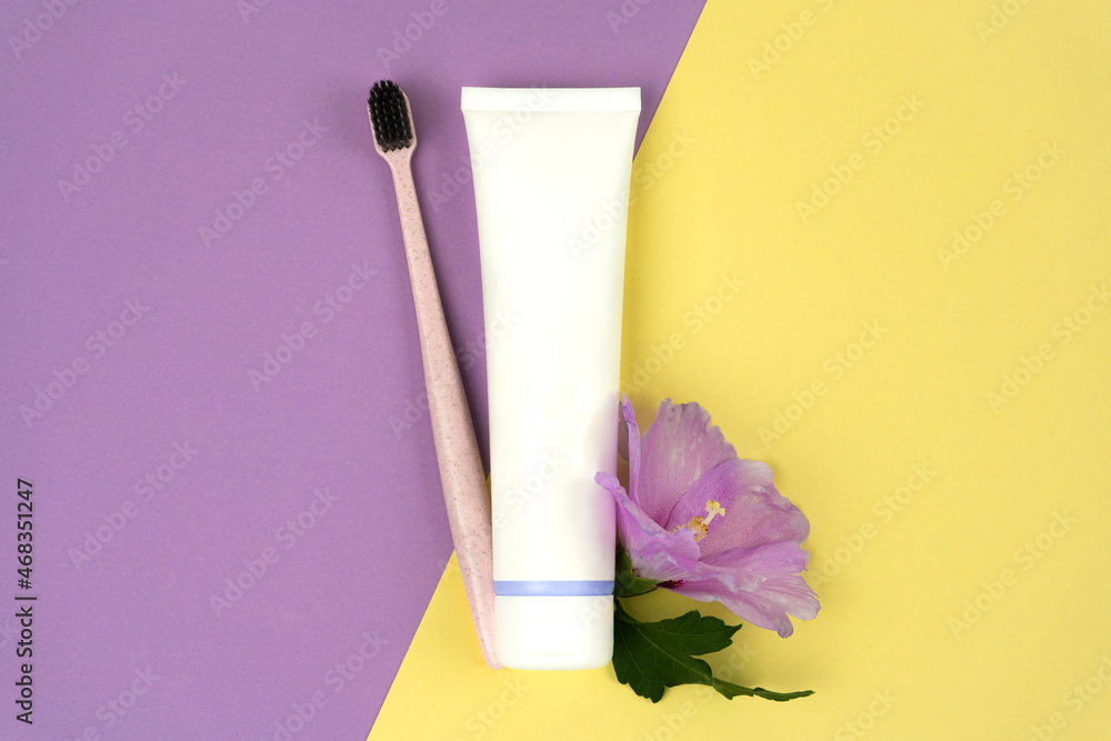 Tube of toothpaste with a toothbrush made of recycled plastic with purple flower on colored backgrounds. Eco consumption concept Tube of toothpaste with a toothbrush made of recycled plastic with purple flower on colored backgrounds. Eco consumption concept