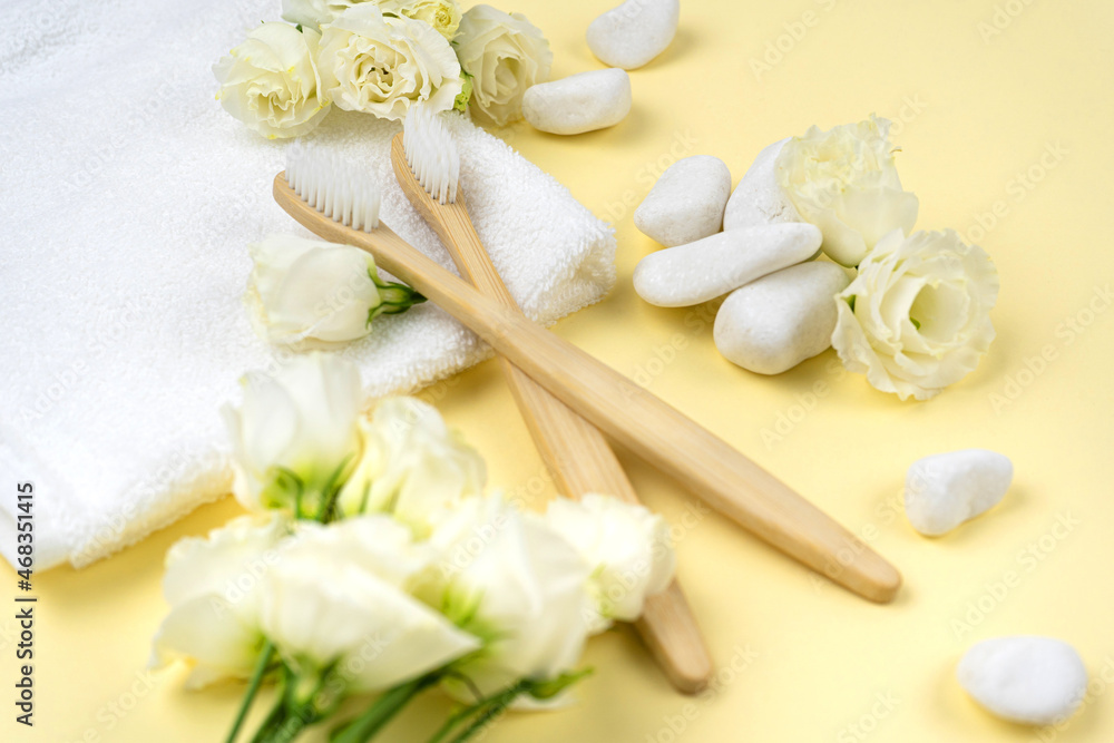 Natural bamboo toothbrushes on a towel next to white stone with a flower on yellow background. The concept of zero waste, no plastic Natural bamboo toothbrushes on a towel next to white stone with a flower on yellow background. The concept of zero waste, no plastic
