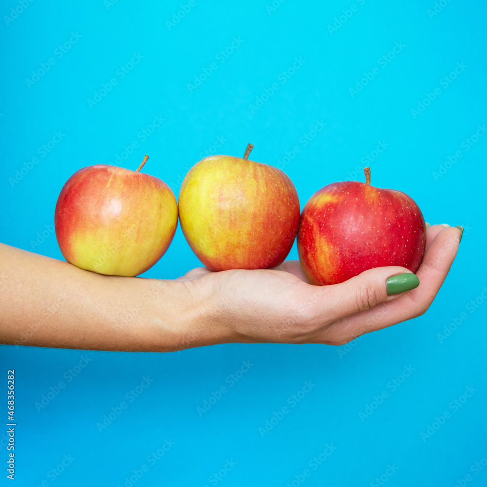 an apple in palm of woman's hand. girl holds red apples on her hand on blue background. three ripe apples on his hand. green manicure. square image an apple in palm of woman's hand. girl holds red apples on her hand on blue background. three ripe apples on his hand. green manicure. square image