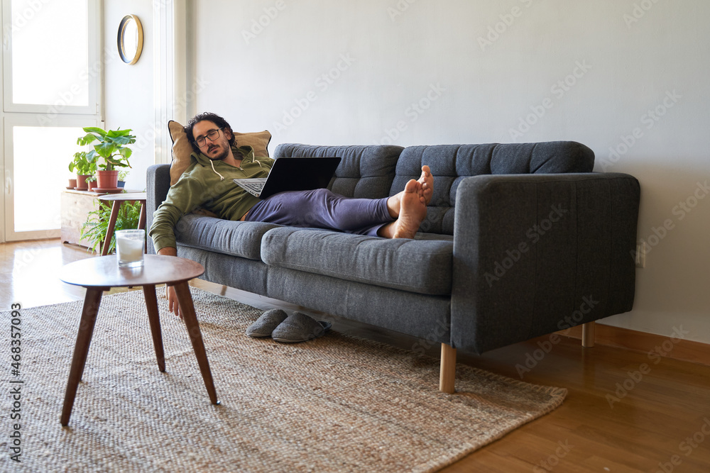 Wide shot of young man sleeping on the sofa while working with laptop Wide shot of young man sleeping on the sofa while working with laptop
