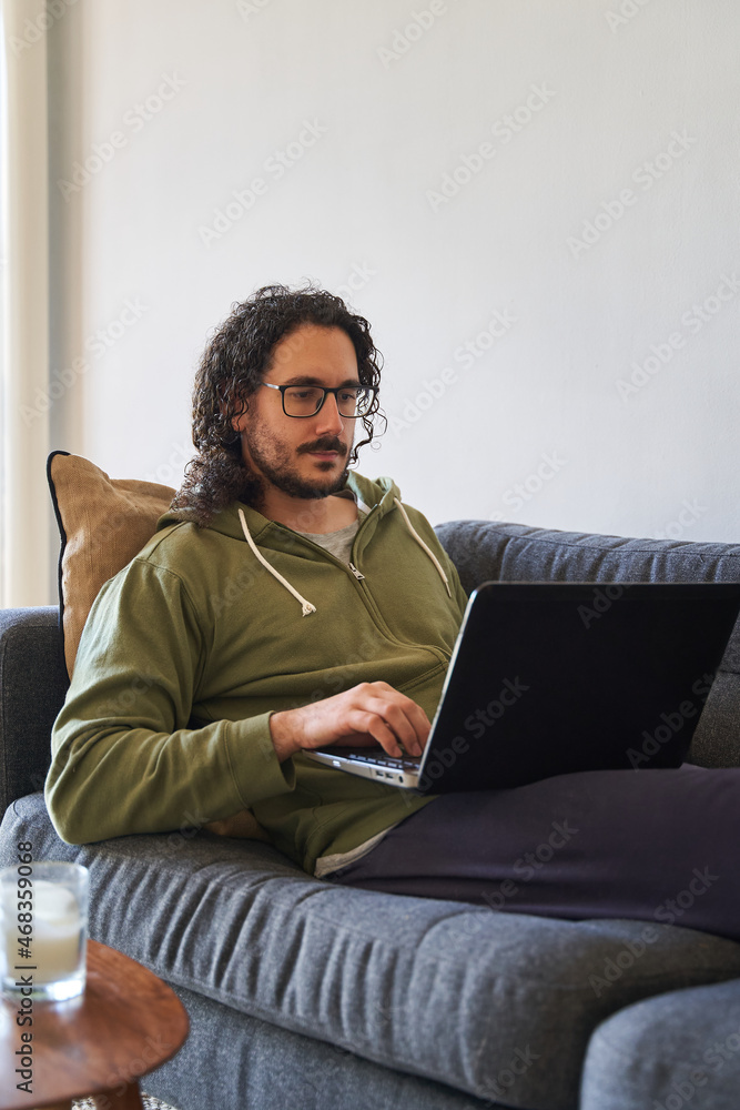 Vertical medium shot of young man using laptop on the sofa Vertical medium shot of young man using laptop on the sofa