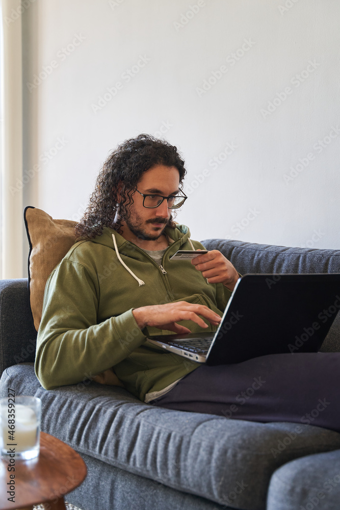 Vertical medium shot of online shopping concept with young man using credit card and laptop on the sofa Vertical medium shot of online shopping concept with young man using credit card and laptop on the sofa