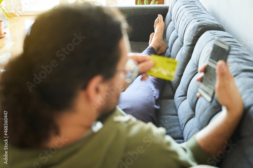 Online shopping concept with young man out of focususing credit card and smartphone on the sofa