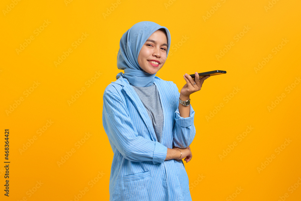 Smiling young Asian woman talking on mobile phone and looking at camera over yellow background Smiling young Asian woman talking on mobile phone and looking at camera over yellow background