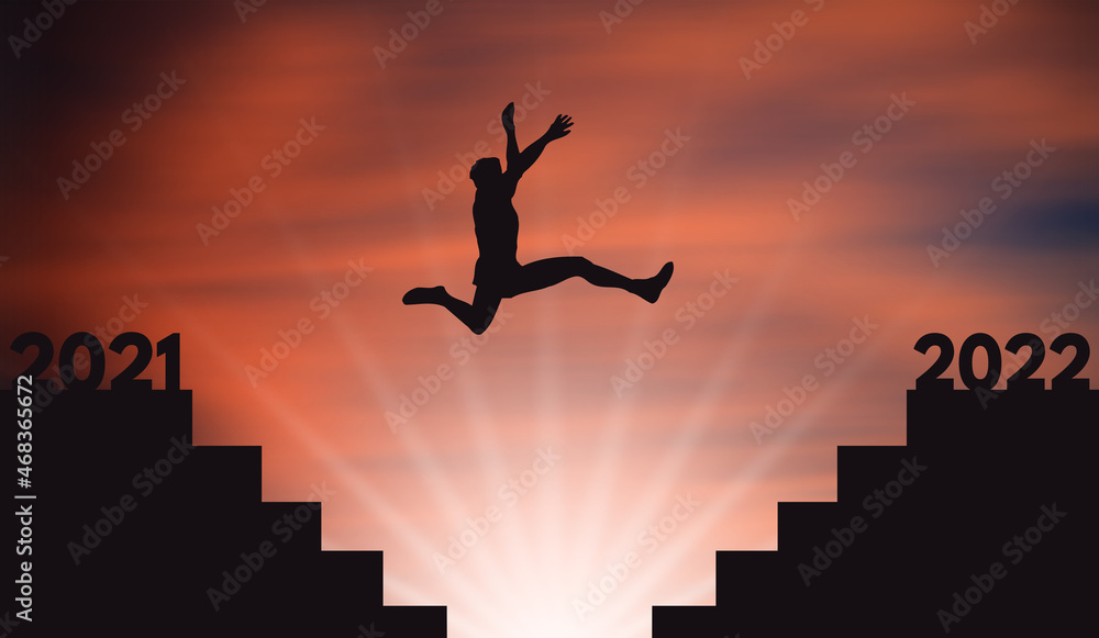 Young Man Jumping  From 2021 To 2022 Over Stairs with a Big Jump at Orange Sunset. Person silhouette Jump on Stair gap From Dark side to light Side. New Year and Success and Hope Concept 