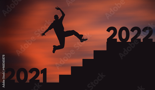 Young Happy Man Jumping To The Highest Stair From 2021 to 2022 at sunset. Silhouette of a Joyful Guy jumps Over Stairs. Success and Futuristic Businessman in 2022 Concept. 