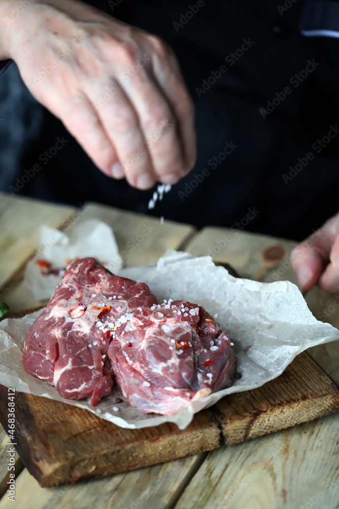 Soft focus. The chef's hand is salting raw lamb. Soft focus. The chef's hand is salting raw lamb.