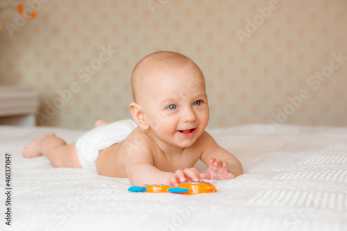 a baby boy in a diaper with a rattle on the bed is lying on his stomach