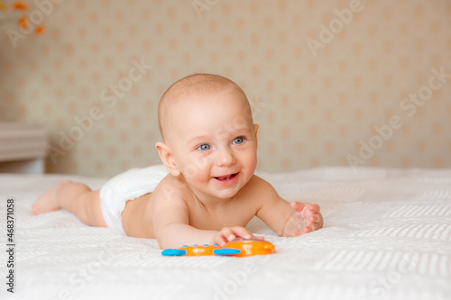 a baby boy in a diaper with a rattle on the bed is lying on his stomach