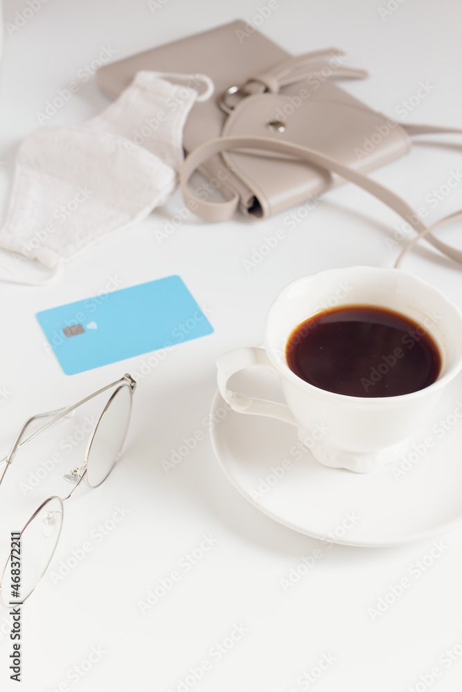 Cup of coffee, credit card, glasses, purse and mask on white table. Cafe, restaurant on pandemic concept. Cup of coffee, credit card, glasses, purse and mask on white table. Cafe, restaurant on pandemic concept.