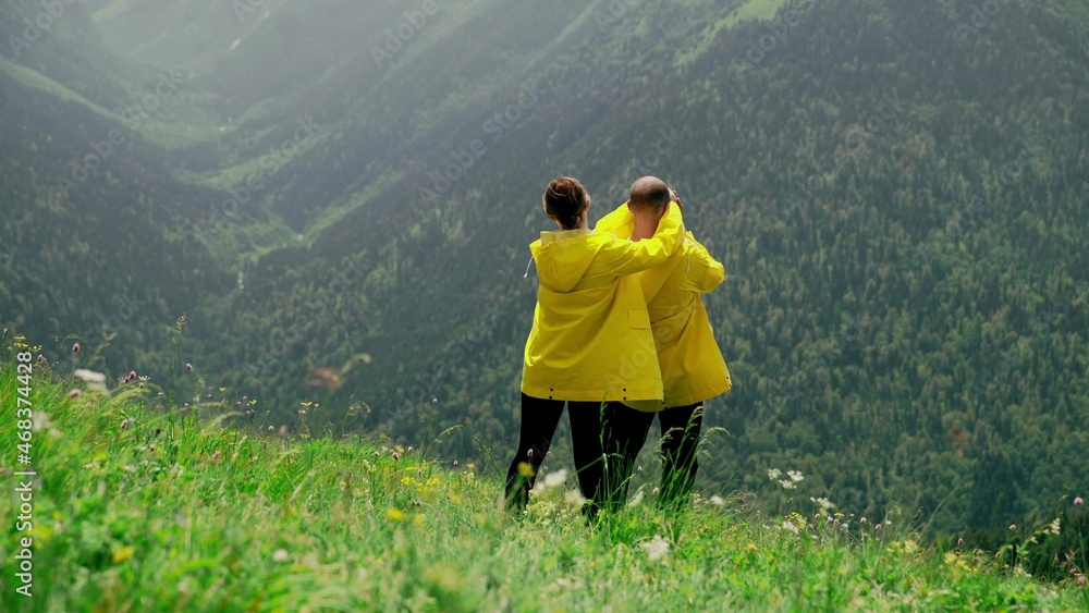 A young woman in a yellow raincoat goes down the slope to a man and covers his eyes with her hands, a young couple rejoices at each other. Travel and tourism