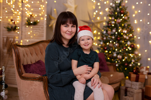 Mom and daughter sitting on a couch at home near the Christmas tree © Di Studio