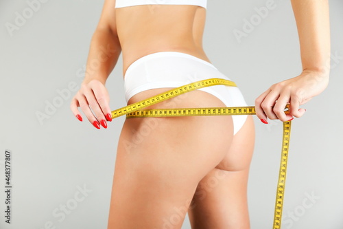 sport woman wearing white underwear holds measuring tape on gray background. athlete woman measures her buttocks with measuring tape