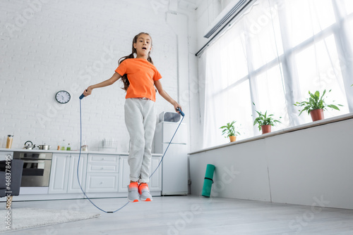 Low angle view of kid jumping with skipping rope in kitchen