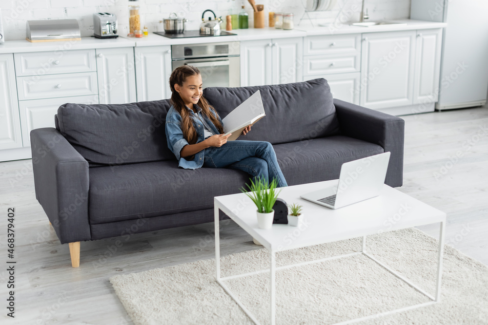 Smiling preteen child holding notebook near laptop on coffee table at home Smiling preteen child holding notebook near laptop on coffee table at home