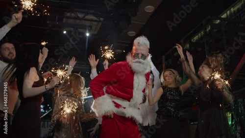 Santa on New Year indoor party dancing with excited women and energetic men.
