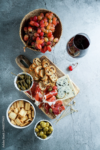 traditional Spanish or Italian tapas. jamon iberico, blue cheese, crackers, olives, grapes and dry red wine, grey stone background. Top view