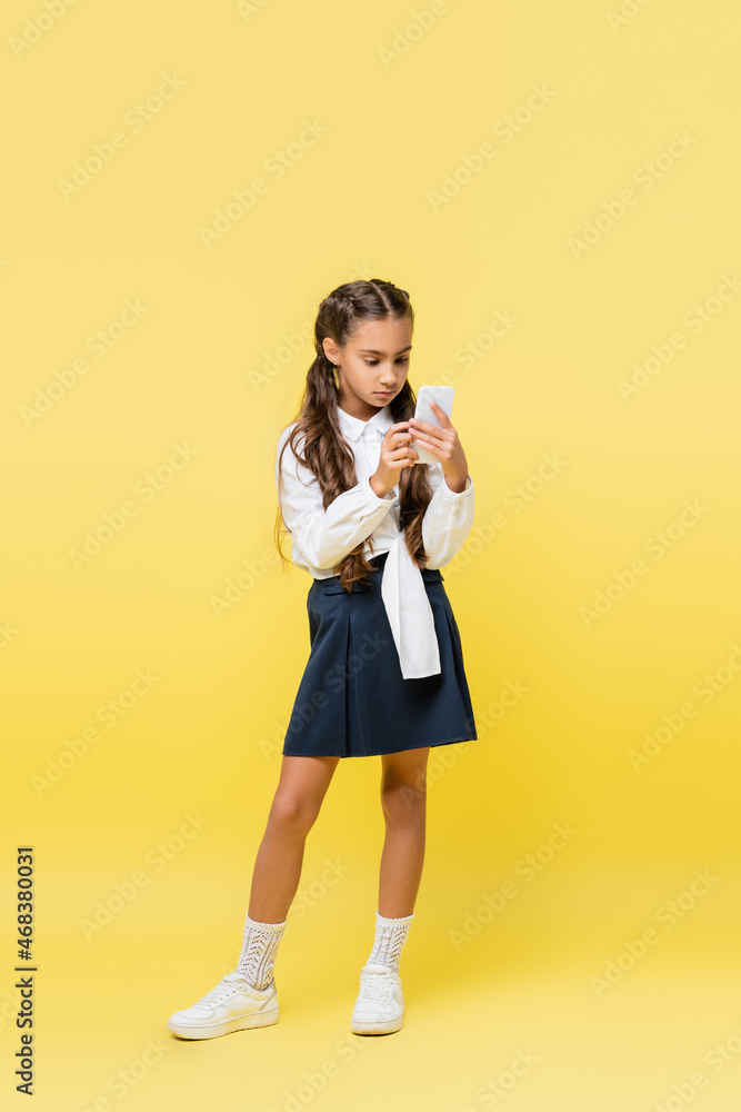 Schoolkid in skirt using mobile phone on yellow background Schoolkid in skirt using mobile phone on yellow background