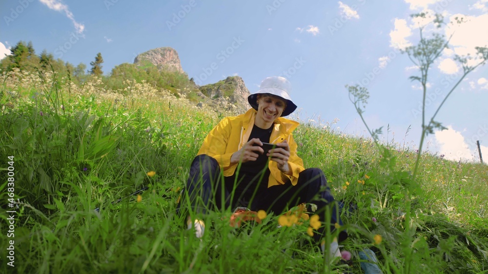 A young man is sitting on a slope and playing a game on his phone in a mountainous area. Tourism and travel A young man is sitting on a slope and playing a game on his phone in a mountainous area. Tourism and travel