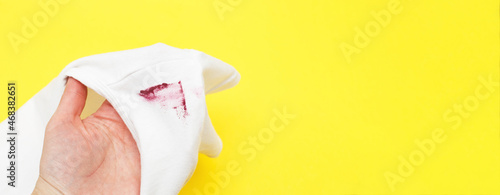 female hand holding white shirt with red lipstick stain on yellow background
