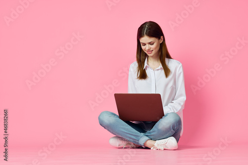 woman with laptop sitting on the floor internet communication online pink background