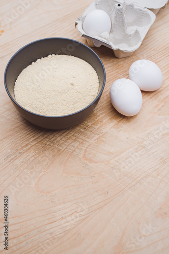 dark gray bowl with whole wheat flour and white eggs on a rustic wooden tabletop