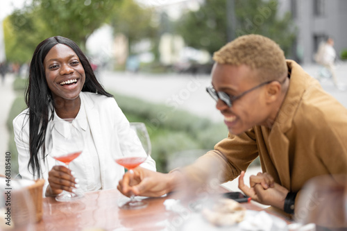 Young african woman and latin man having fun during a business lunch at outdoor cafe. Concept of teambuilding and corporate event. Idea of rest and leisure on job