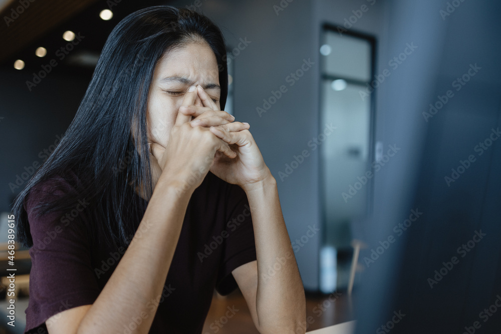 Asian woman closes her eyes and massages her nose while sitting at work Feeling tired and stressed Asian woman closes her eyes and massages her nose while sitting at work Feeling tired and stressed