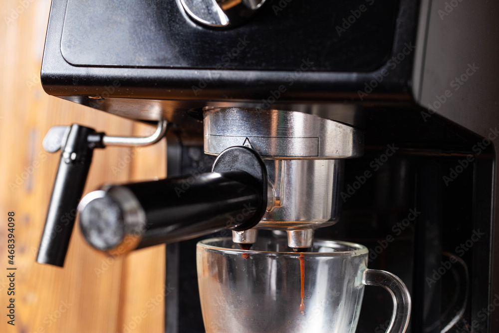 Making coffee in a coffee machine in the kitchen, close-up. Black coffee flowing into a transparent cup on a wooden table top background Making coffee in a coffee machine in the kitchen, close-up. Black coffee flowing into a transparent cup on a wooden table top background