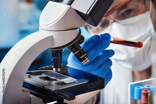 Microscopist scientist examining a blood sample under a microscope infected with covid-19 in the laboratory. Doctor with blood tube with a new strain of coronavirus in the microbiology lab