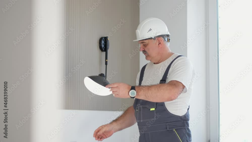 An elderly electrician checks the operation of the wall sconces of the lamp in the house after installation and repair An elderly electrician checks the operation of the wall sconces of the lamp in the house after installation and repair