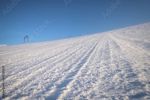 Snow-covered slope for skiers and snowboarders. Against the background of the blue sky on a clear sunny day. Drawing of wind and frost.
