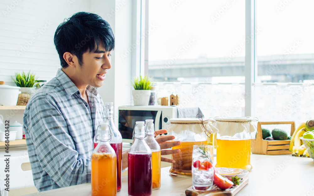Portrait handsome man smiling with fresh and happiness, recommending Kombucha healthy fermented probiotic tea drinks with ingredients red apples, strawberries, mushroom scoby in kitchen at home. Portrait handsome man smiling with fresh and happiness, recommending Kombucha healthy fermented probiotic tea drinks with ingredients red apples, strawberries, mushroom scoby in kitchen at home.