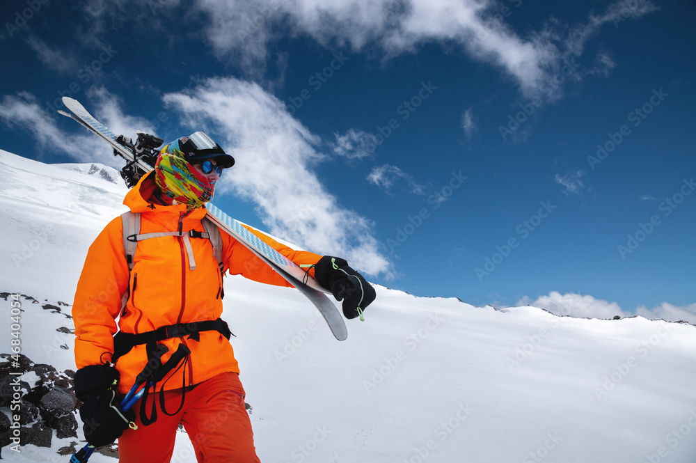 Mountain portrait of a professional freeride skier in orange clothing with  ski poles and skis on his shoulders. Stands high in the mountains on a  snowy slope foto de Stock | Adobe