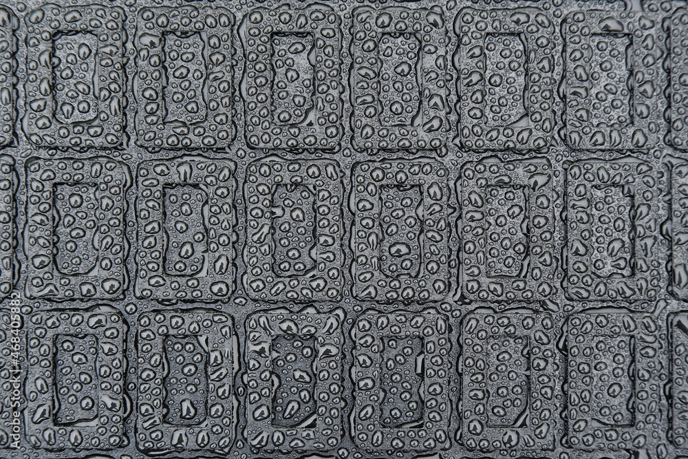 The texture of a black rubber car mat in water droplets.Abstract geometric image on a rubber base.