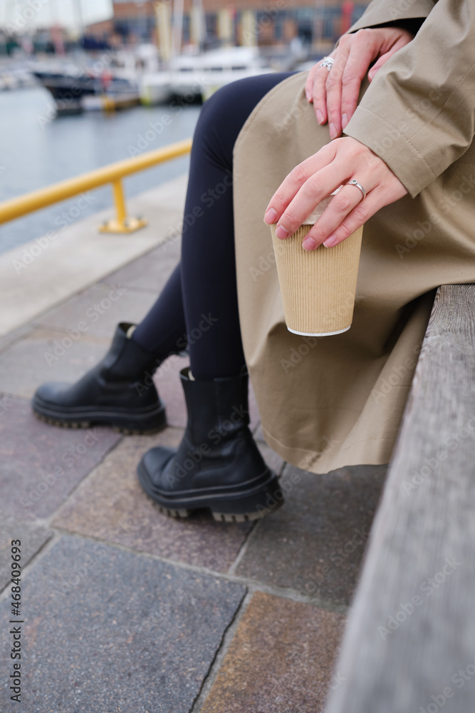Girl drinks coffee on the background of yachts in the Marina. Hot drink in a paper cup. Disposable paper cup close up. Empty space for text, layout Girl drinks coffee on the background of yachts in the Marina. Hot drink in a paper cup. Disposable paper cup close up. Empty space for text, layout