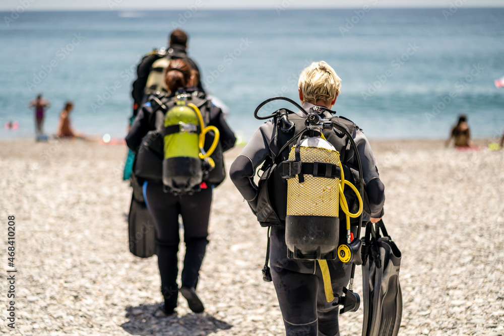 Three scuba divers with all equipment heading to the sea, Spain - obrazy, fototapety, plakaty 