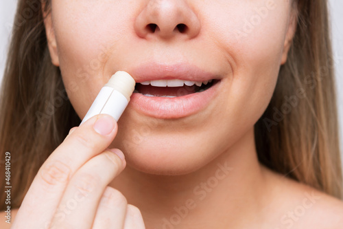Cropped shot of a young caucasian beautiful blonde woman applying a hygienic lipstick on her lips on a white background. Moisturizing chapstick for dry lips