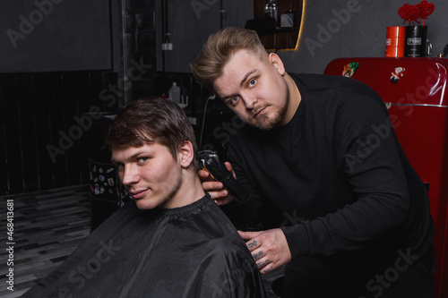 Barber European looking man hairdresser cuts the client with dark hair. Hairdressing