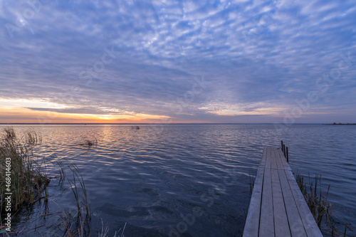 Colorful sunrise on the shore of an autumn lake with a wooden pier. Autumn landscape with a lake in the early morning. A bright streak of light on the horizon, dawn.